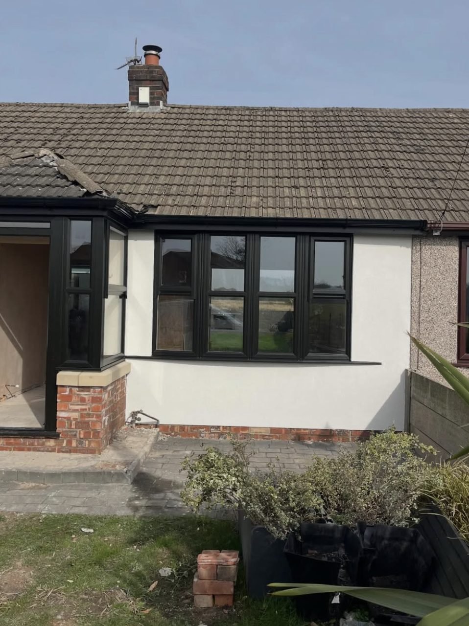 Bungalow front elevation rendered white beside the untouched pebbledash next door